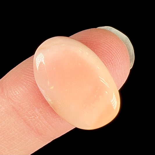 A loose, oval cabochon cut Peruvian opal stone.  The opal is a coral pink color.