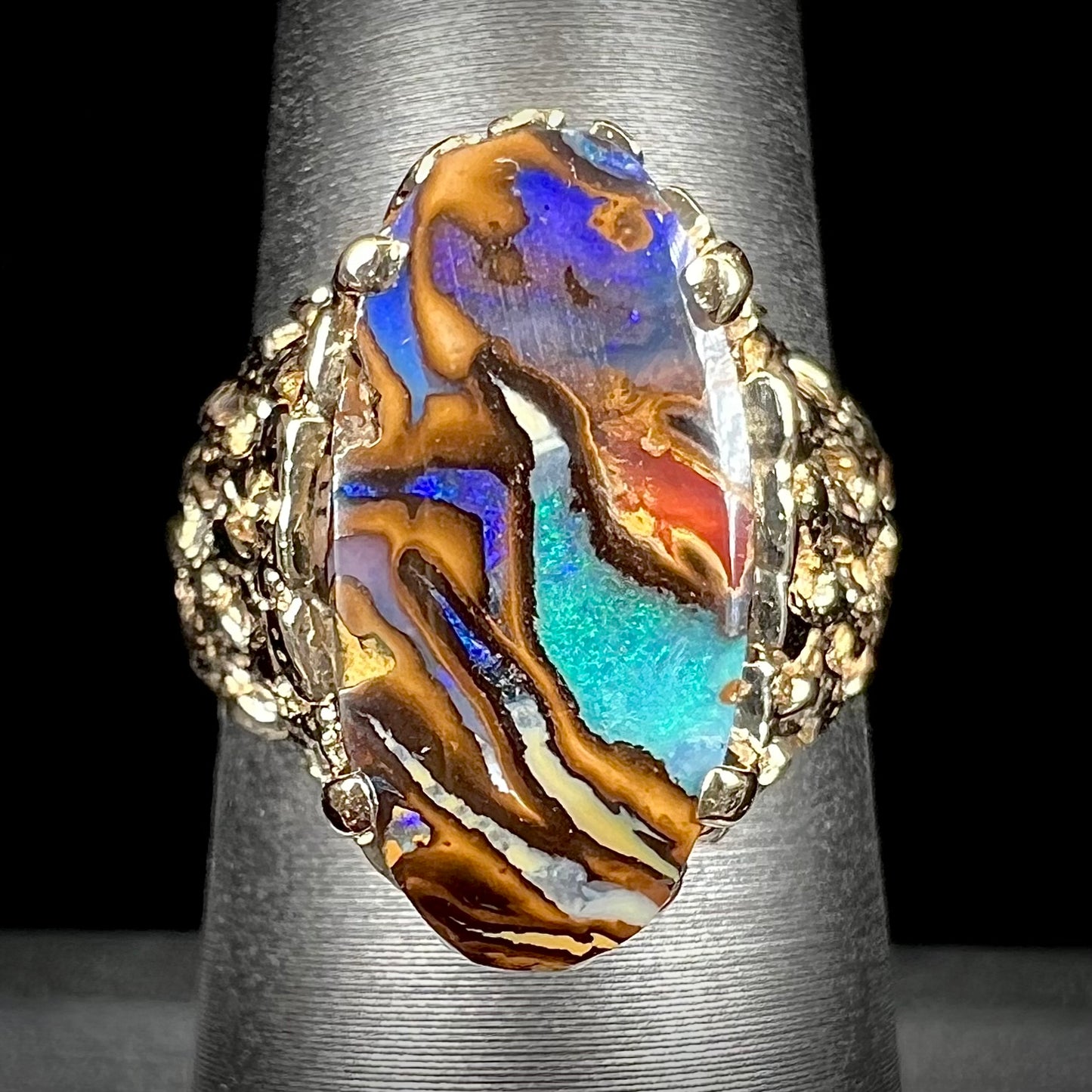 A yellow gold solitaire ring mounted with a Koroit boulder opal stone that shows the picture of a peacock.