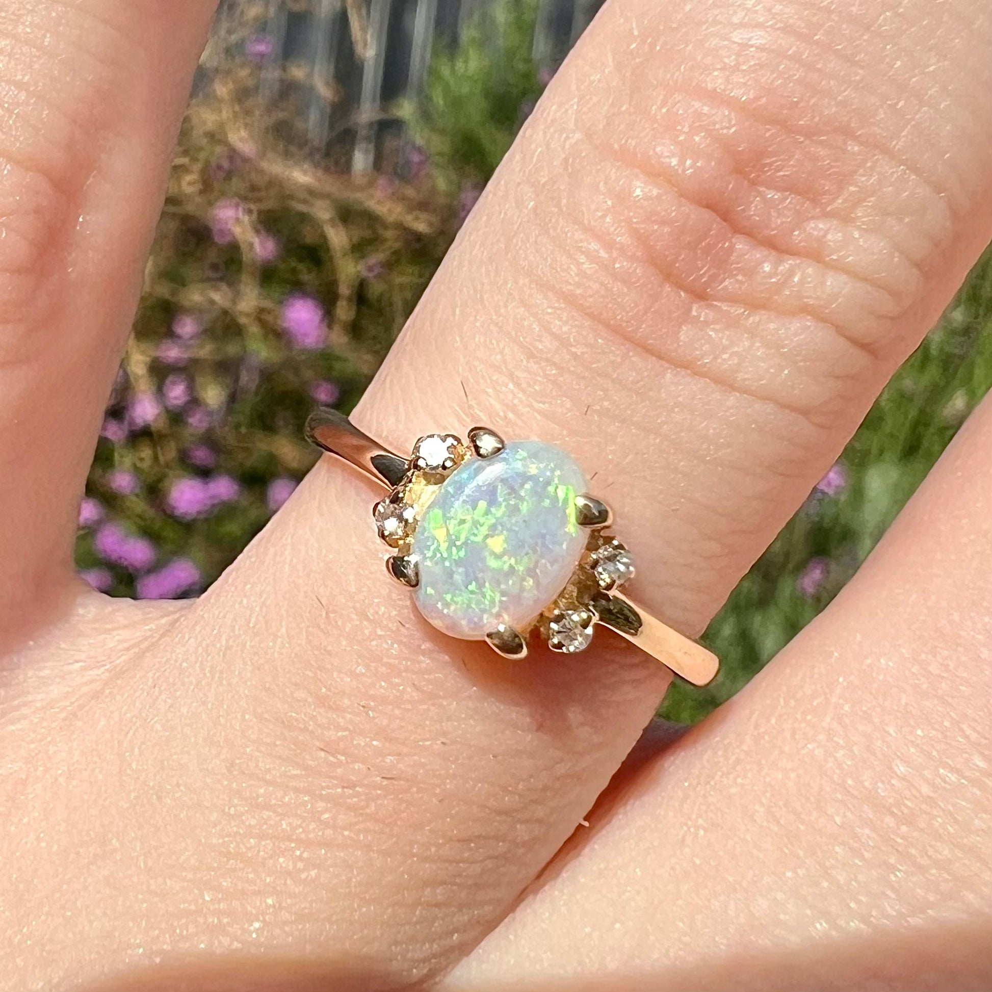 A dainty yellow gold ring set with a Coober Pedy opal with green flashfire pattern and diamond accents.