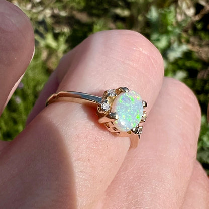 A dainty yellow gold ring set with a Coober Pedy opal with green flashfire pattern and diamond accents.