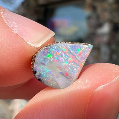 A freeform shaped boulder opal stone with red and blue color play.