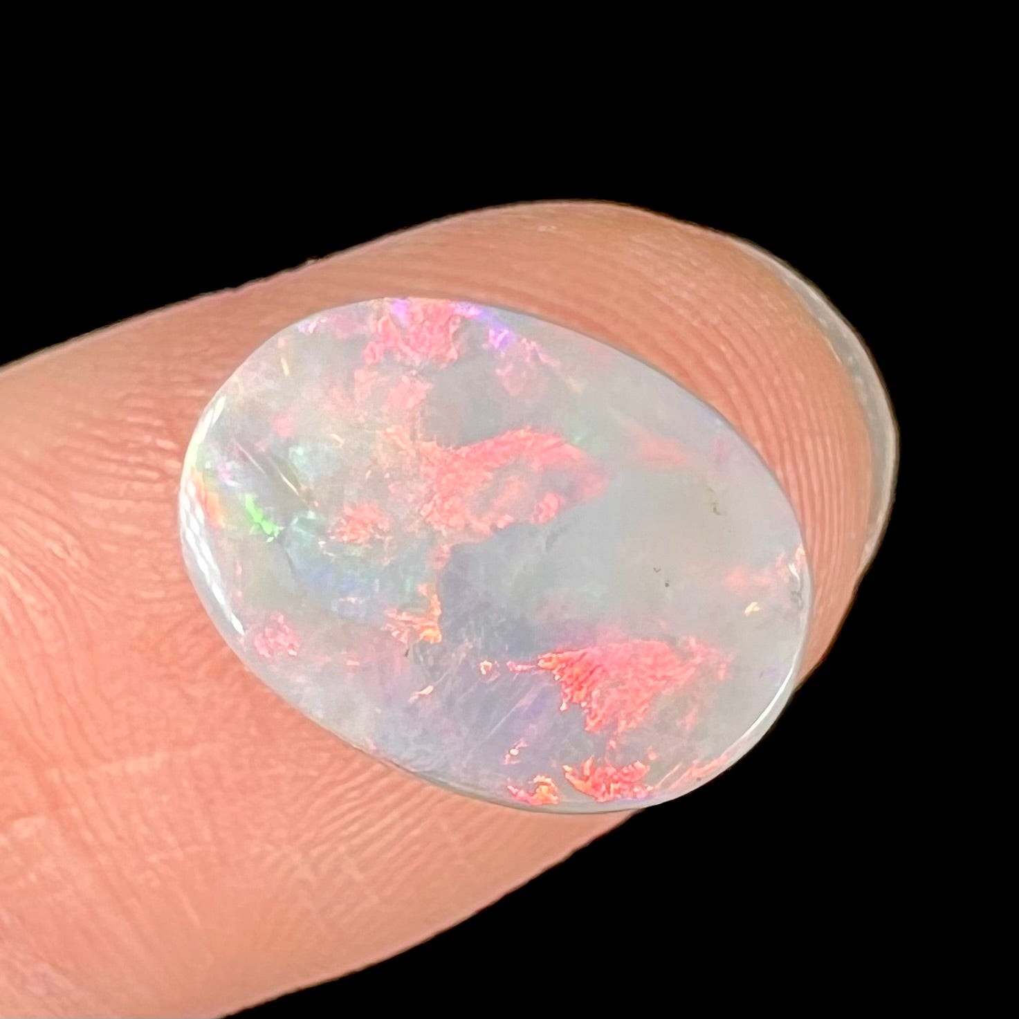 A loose oval cut opal stone from Lightning Ridge, Australia.  The opal shines pinkish red colors.