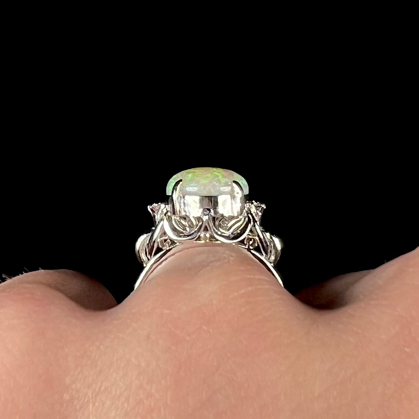 An Australian crystal opal and diamond engagement ring set in a platinum filigree mounting.  The opal plays green/blue colors and has a crack.