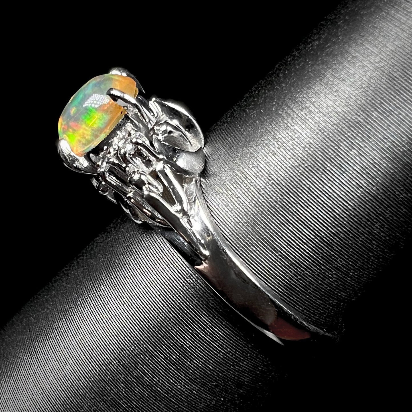 A platinum, diamond accented ring prong-set with an oval cabochon cut Mexican fire opal.