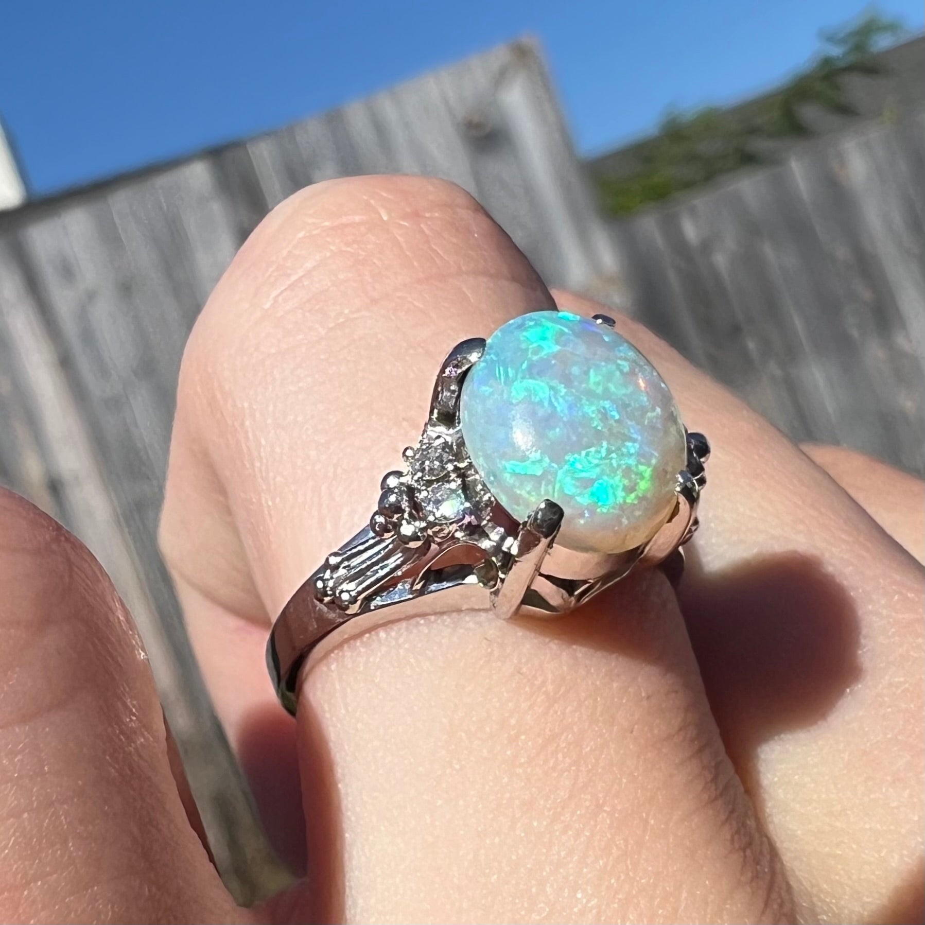 A platinum filigree ring mounted with a blue-green crystal opal and diamond accents.