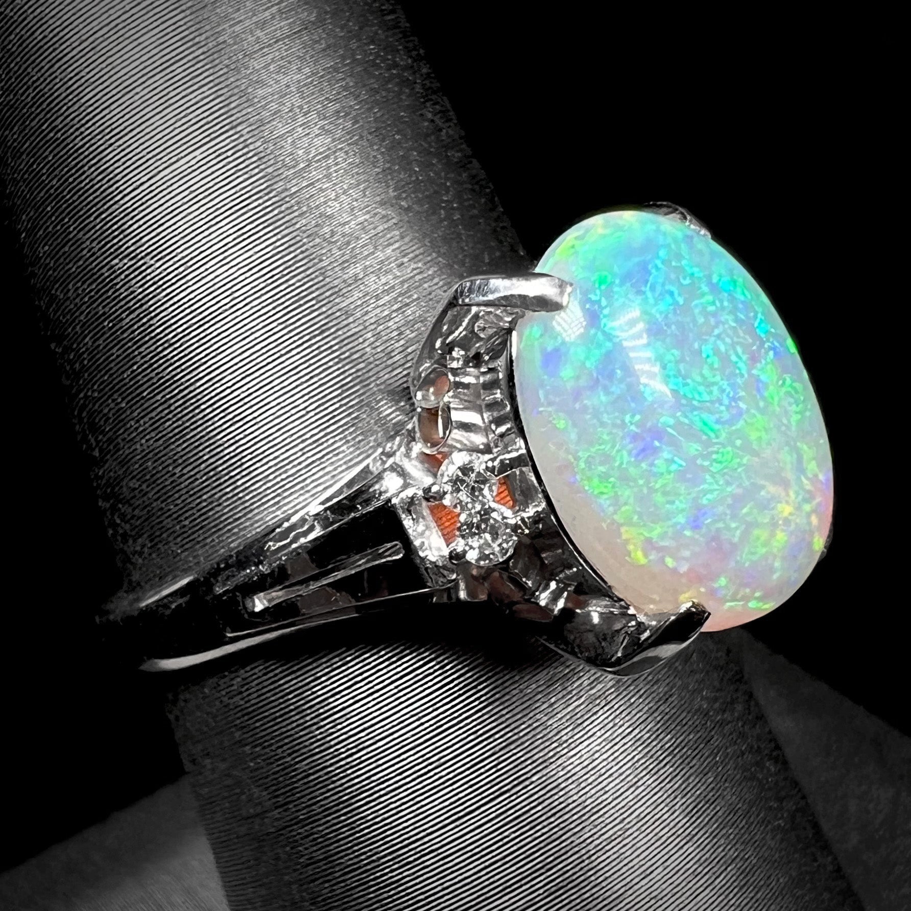 A platinum filigree opal engagement ring set with diamond accents.  The opal has green-blue colors.