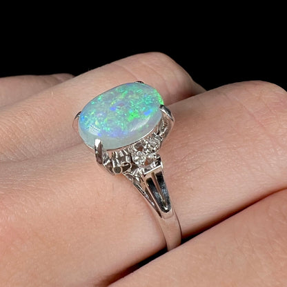 A platinum filigree opal engagement ring set with diamond accents.  The opal has green-blue colors.