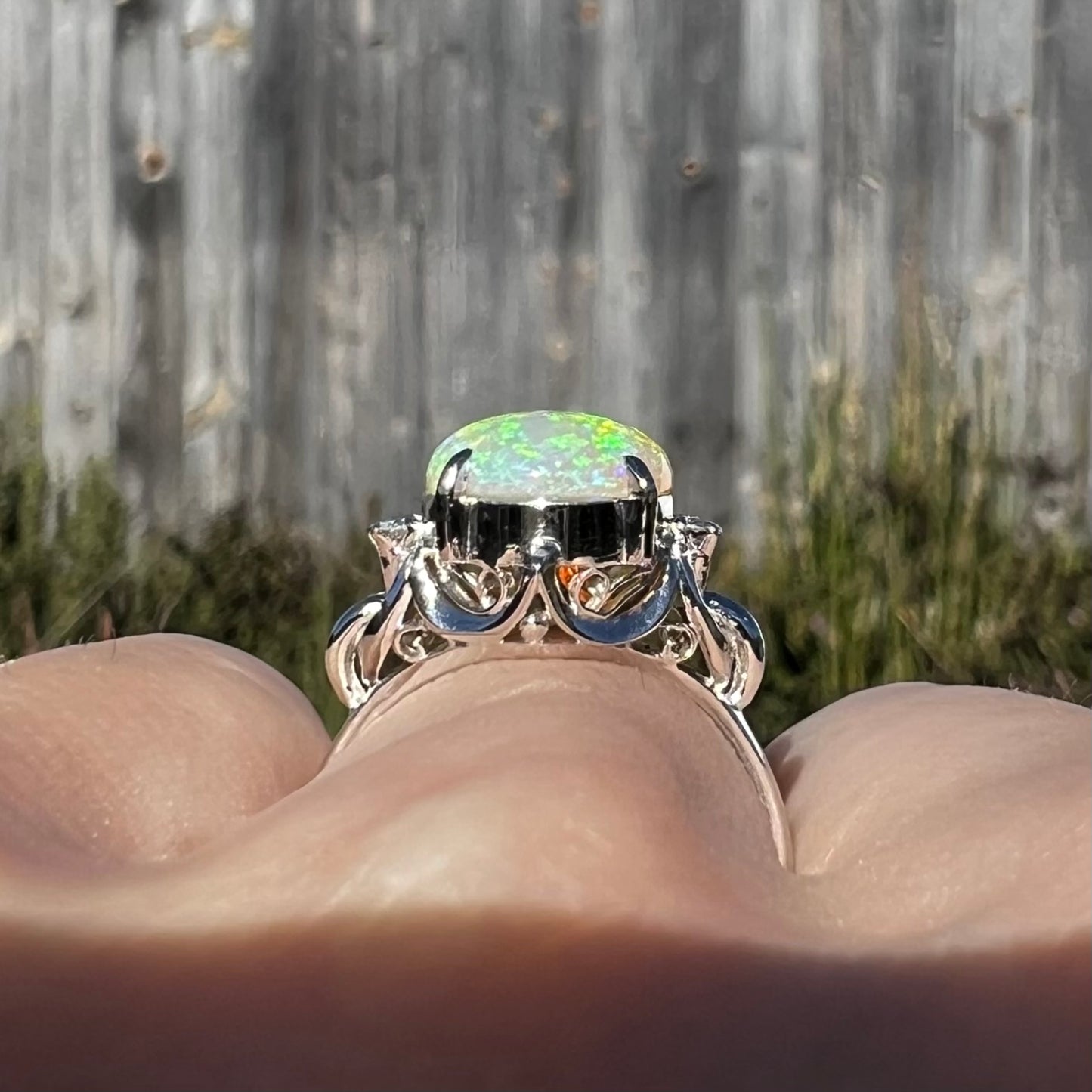 An Australian crystal opal engagement ring set with diamonds in a platinum filigree mounting.  The opal plays green/blue colors and has a crack.