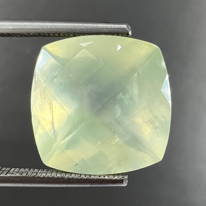 A loose, faceted checkerboard cushion cut green prehnite stone.  The stone is sleepy yellowish green.