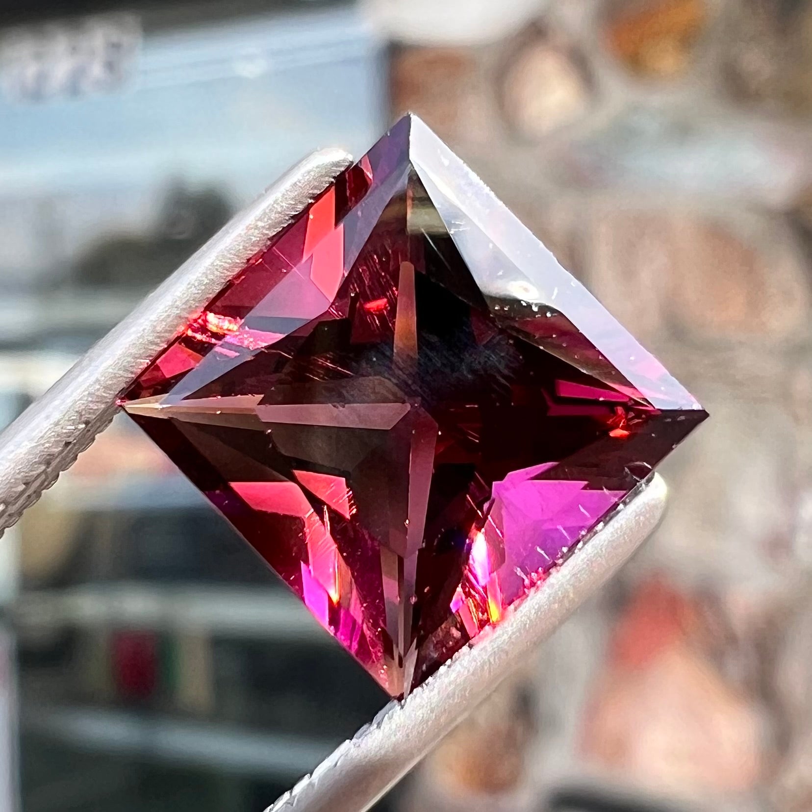 A loose, faceted princess cut tourmaline gemstone.  The stone is a burgundy purple color.