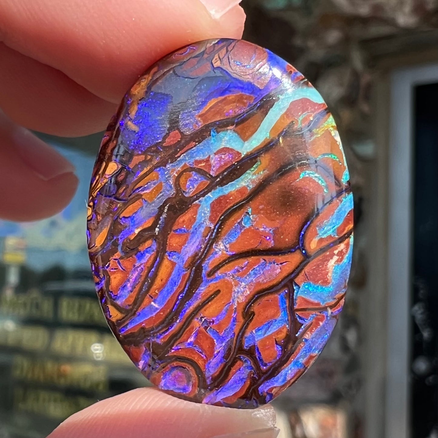 A loose, oval cabochon cut boulder opal from Koroit, Australia.  The opal has violet and purple veins.