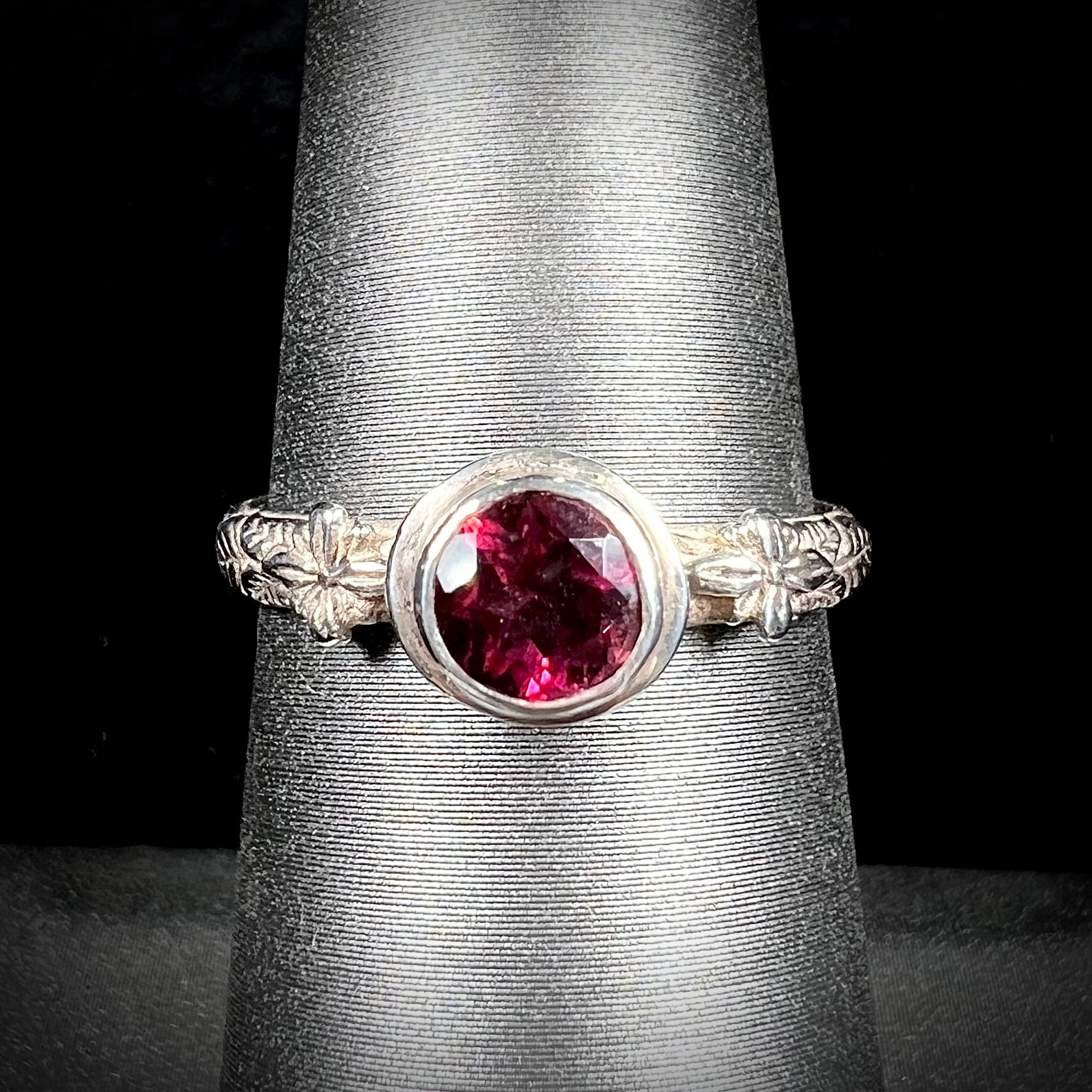 A ladies' sterling silver purple rhodonite garnet solitaire ring.  The shank has an etched floral leaf design.