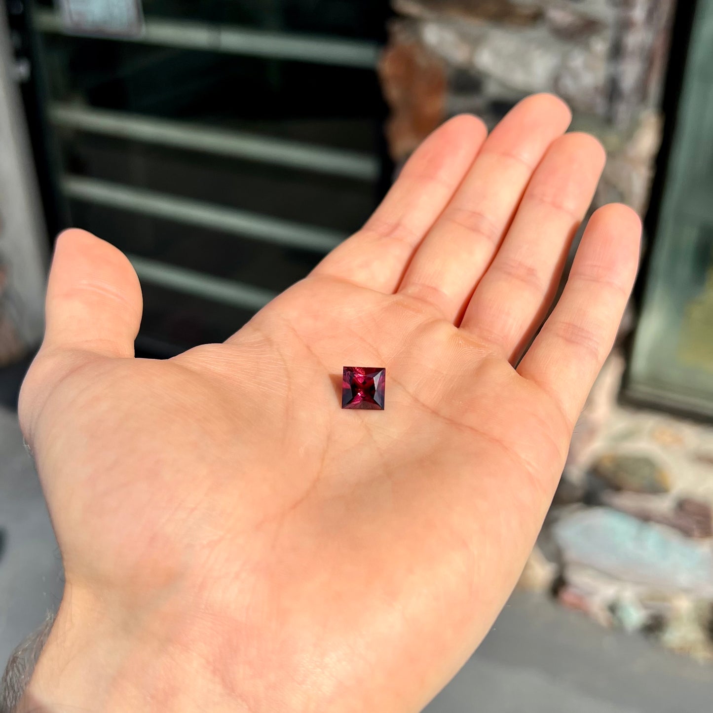 A loose, faceted princess cut tourmaline gemstone.  The stone is a burgundy purple color.