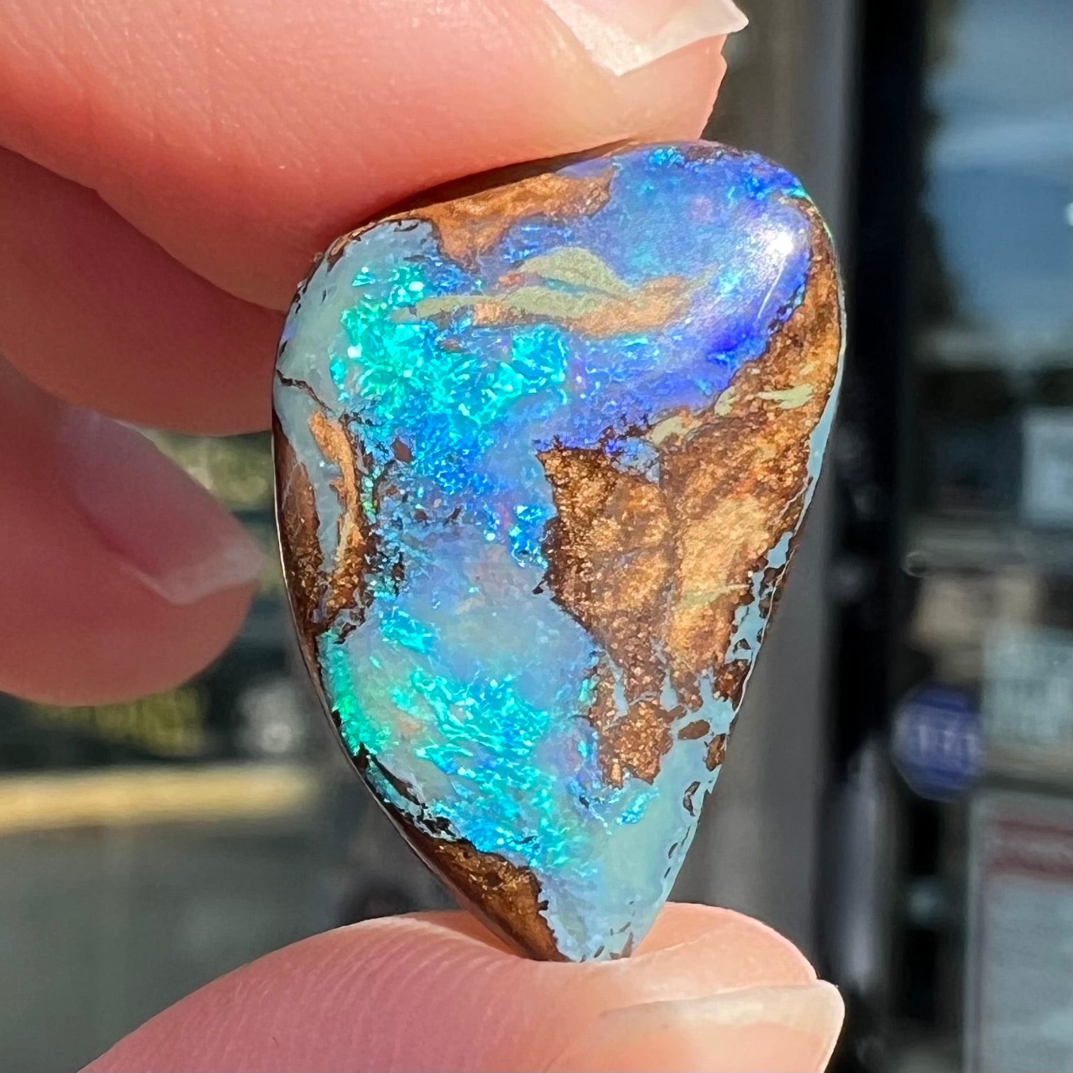 A freeform pear shaped boulder opal stone with blue color.