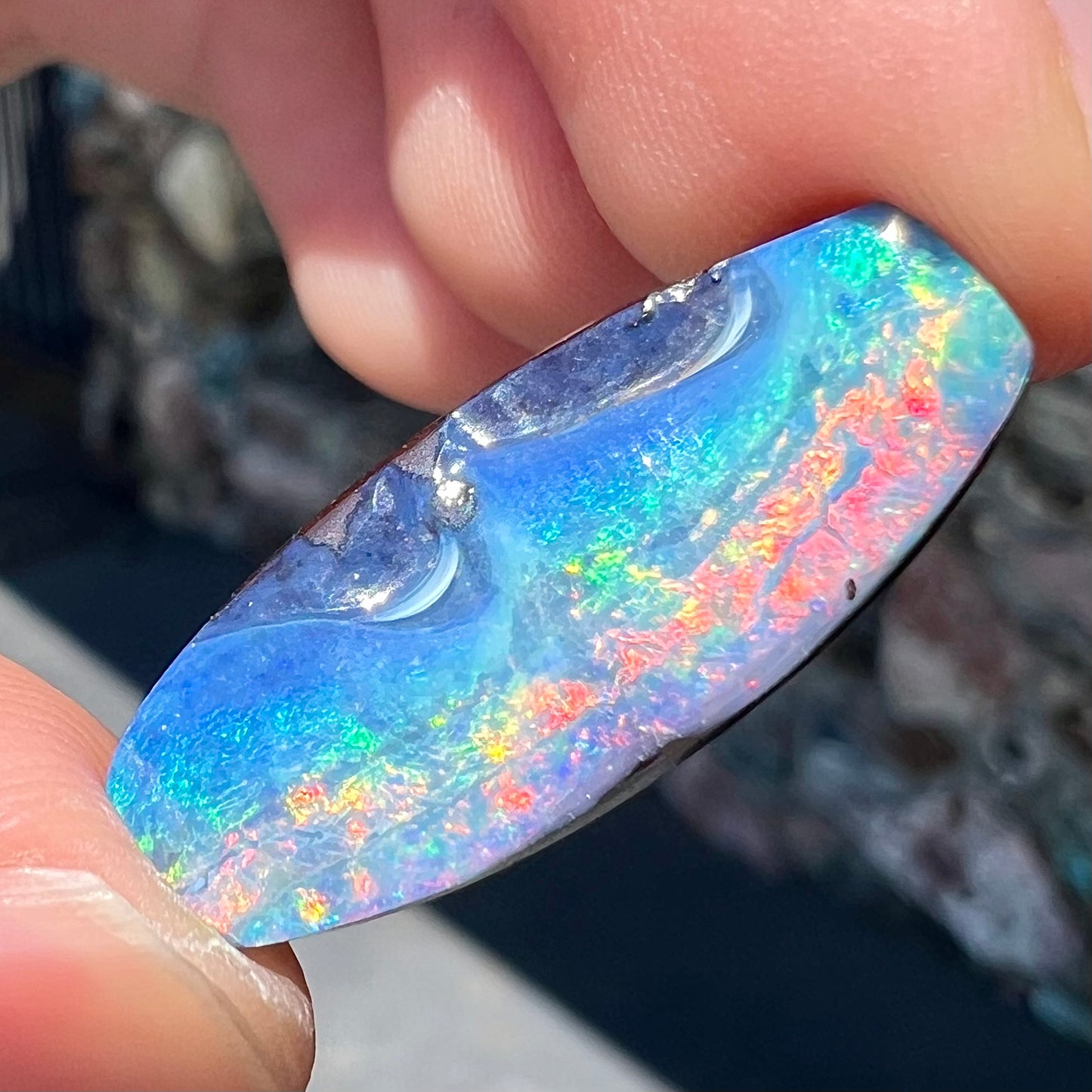 A barrel shaped boulder opal gemstone with a rainbow of colors.