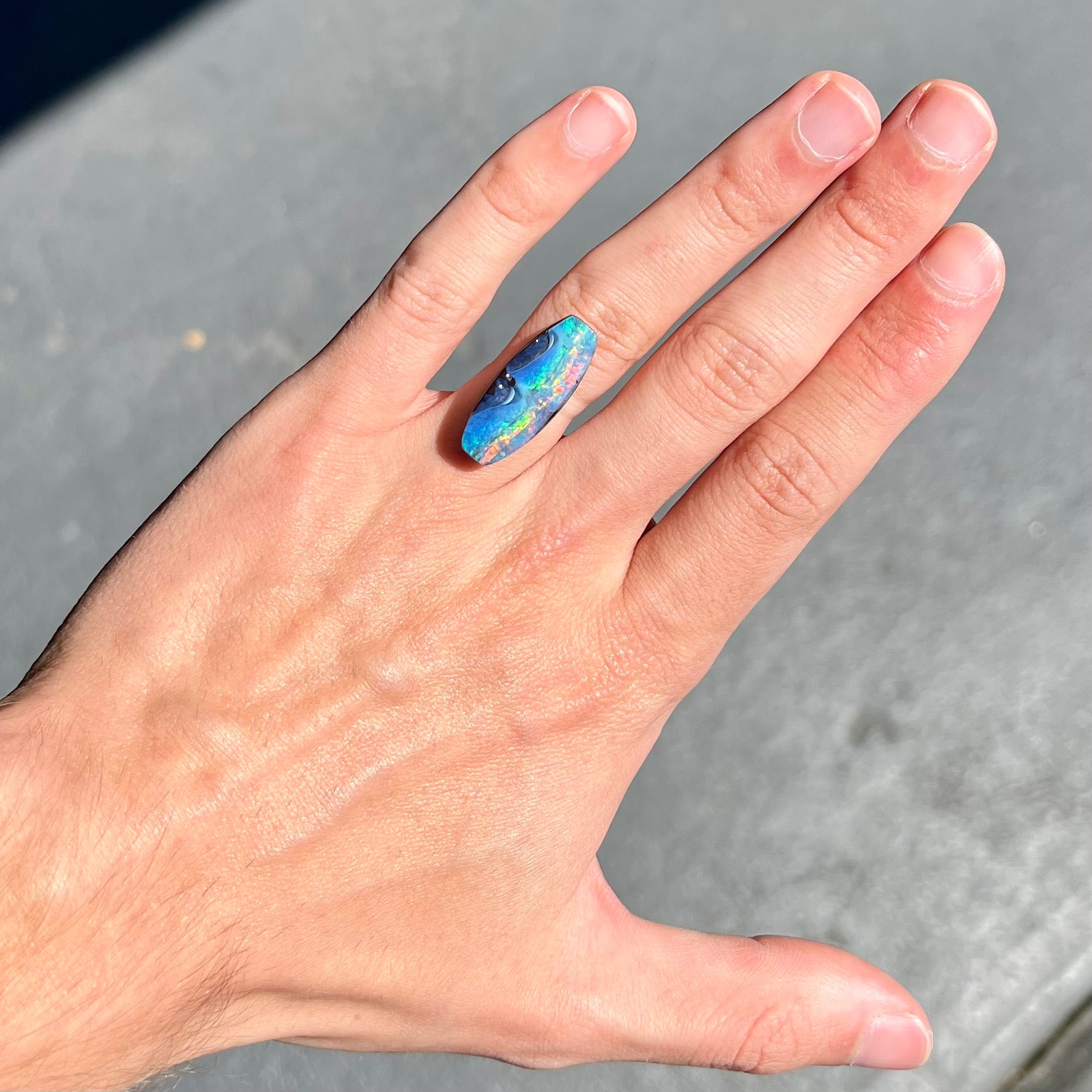 A barrel shaped boulder opal gemstone with a rainbow of colors.