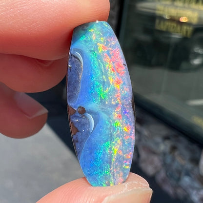 A barrel shaped boulder opal gemstone with a rainbow of colors.