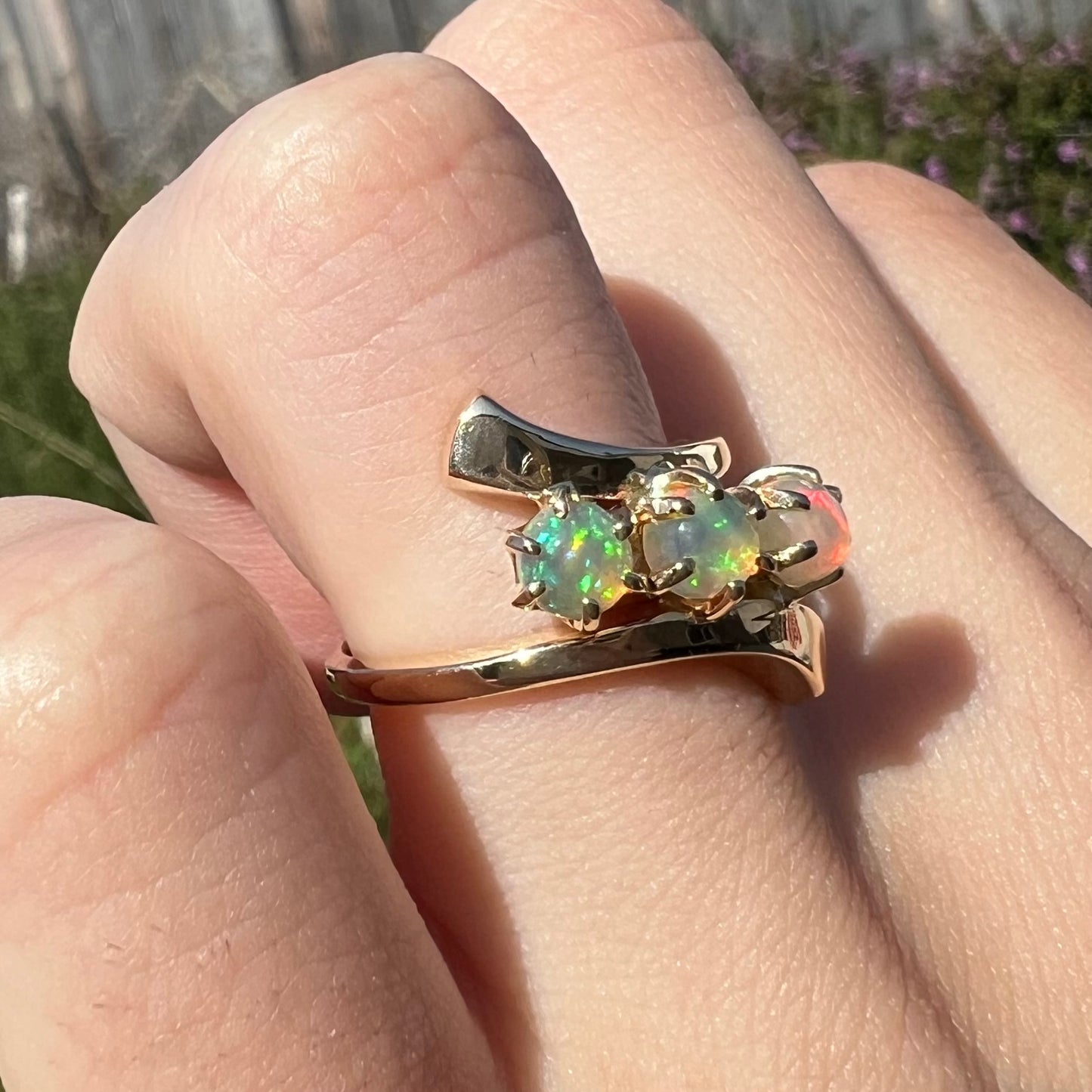 A yellow gold bypass shank ring mounted with three round cabochon cut Ethiopian fire opals.