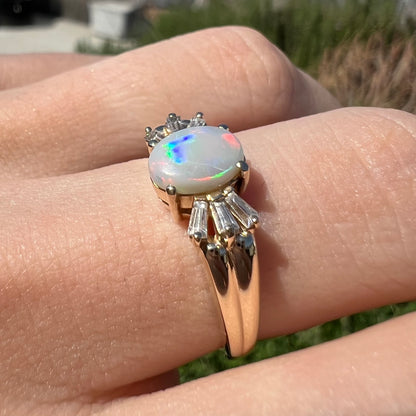 A yellow gold ring set with a natural Australian opal and tapered baguette cut cubic zirconia accents.