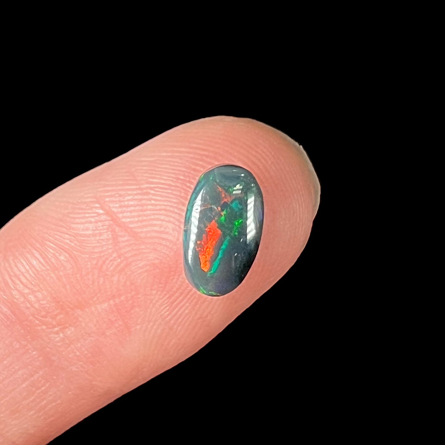 A natural, oval cut black opal stone that shows fire of red, green, and blue.