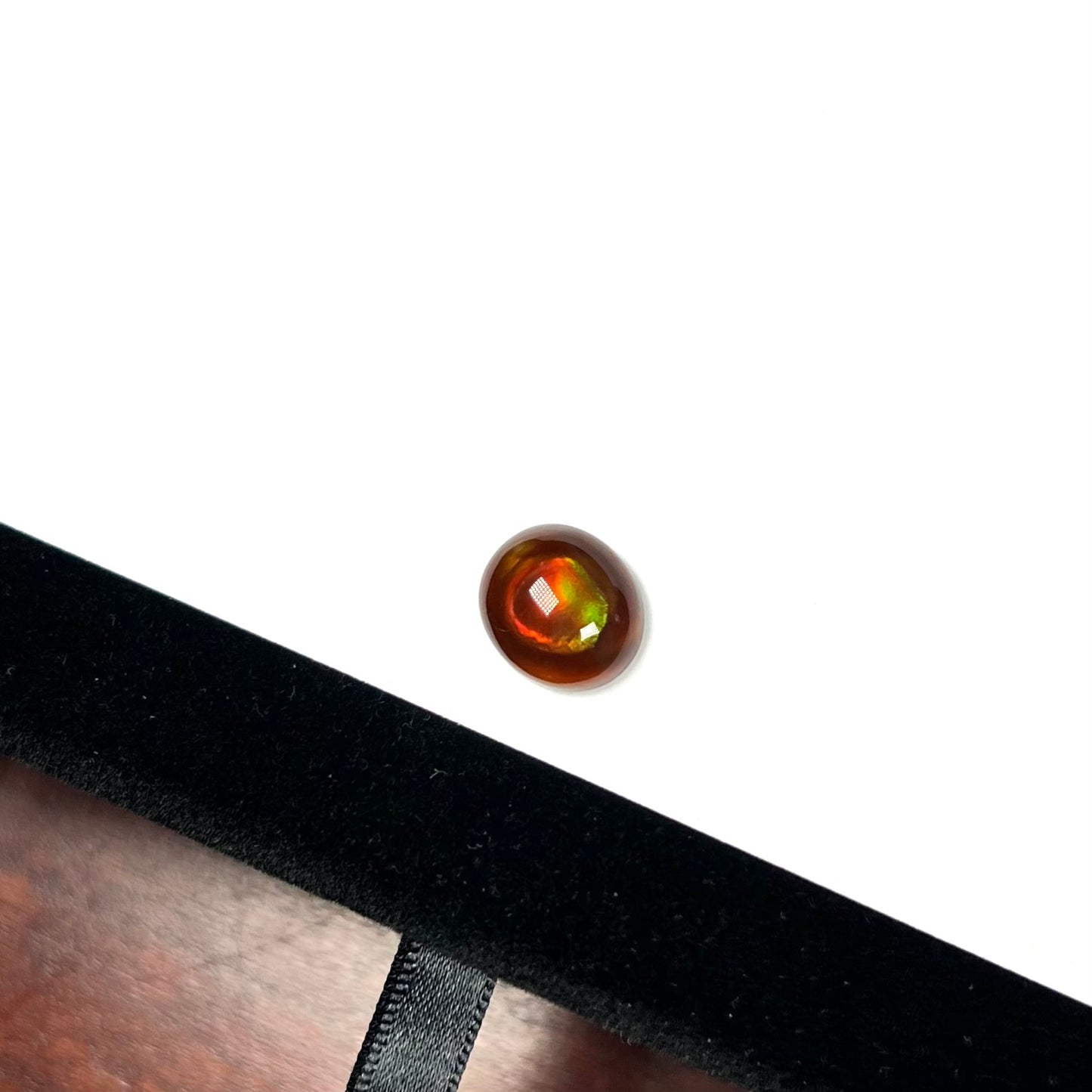 A loose, oval cabochon cut fire agate stone that has red and green colored iridescence.