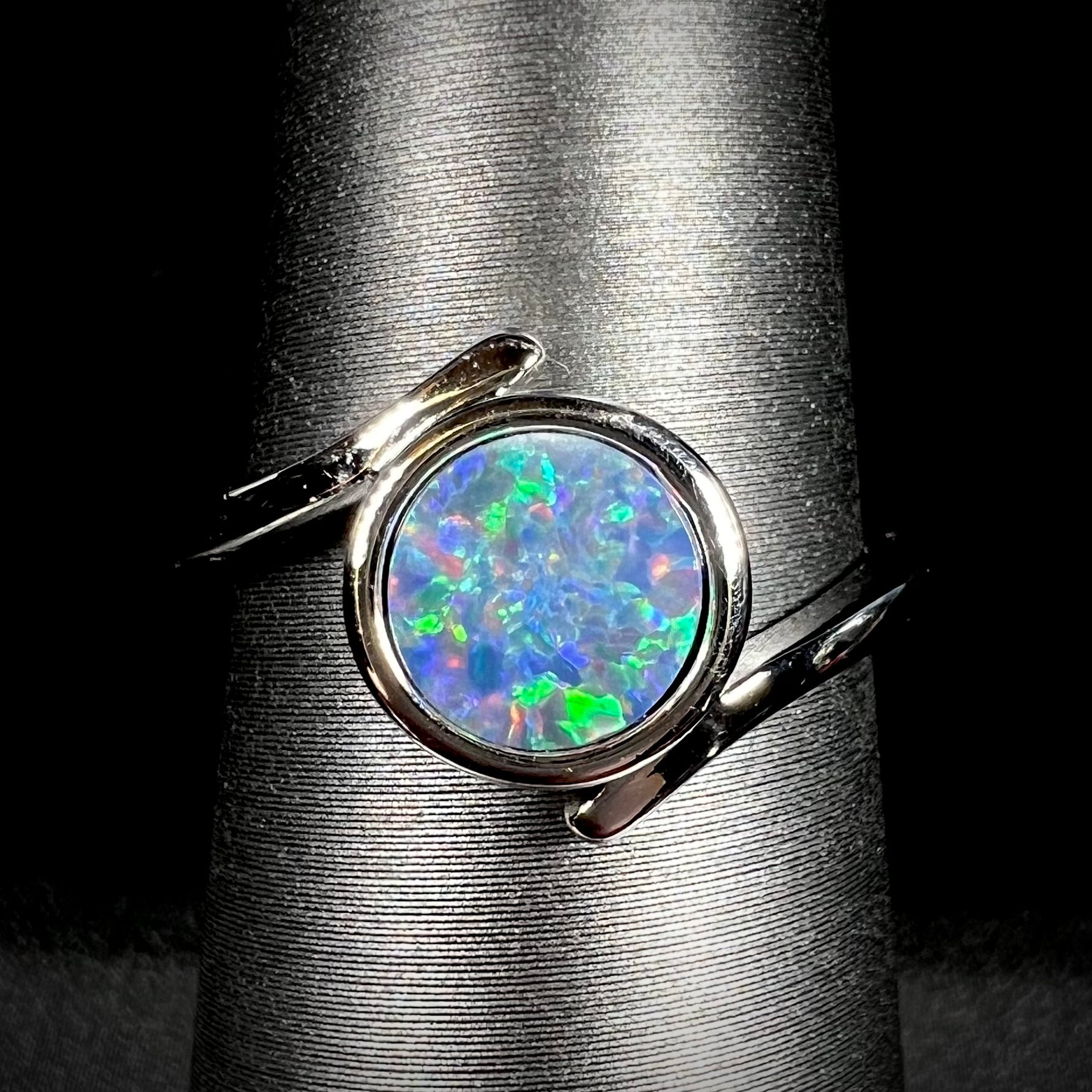 A sterling silver bypass ring bezel-set with a round cut black opal doublet.