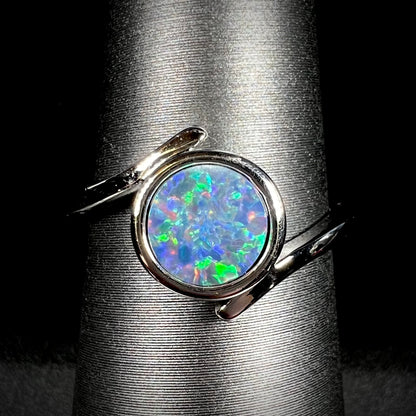 A sterling silver bypass ring bezel-set with a round cut black opal doublet.