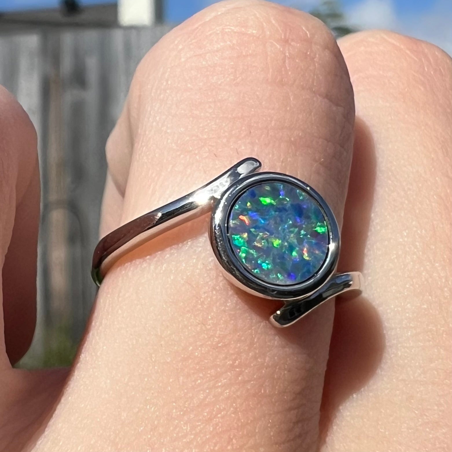 A sterling silver bypass ring bezel-set with a round cut black opal doublet.