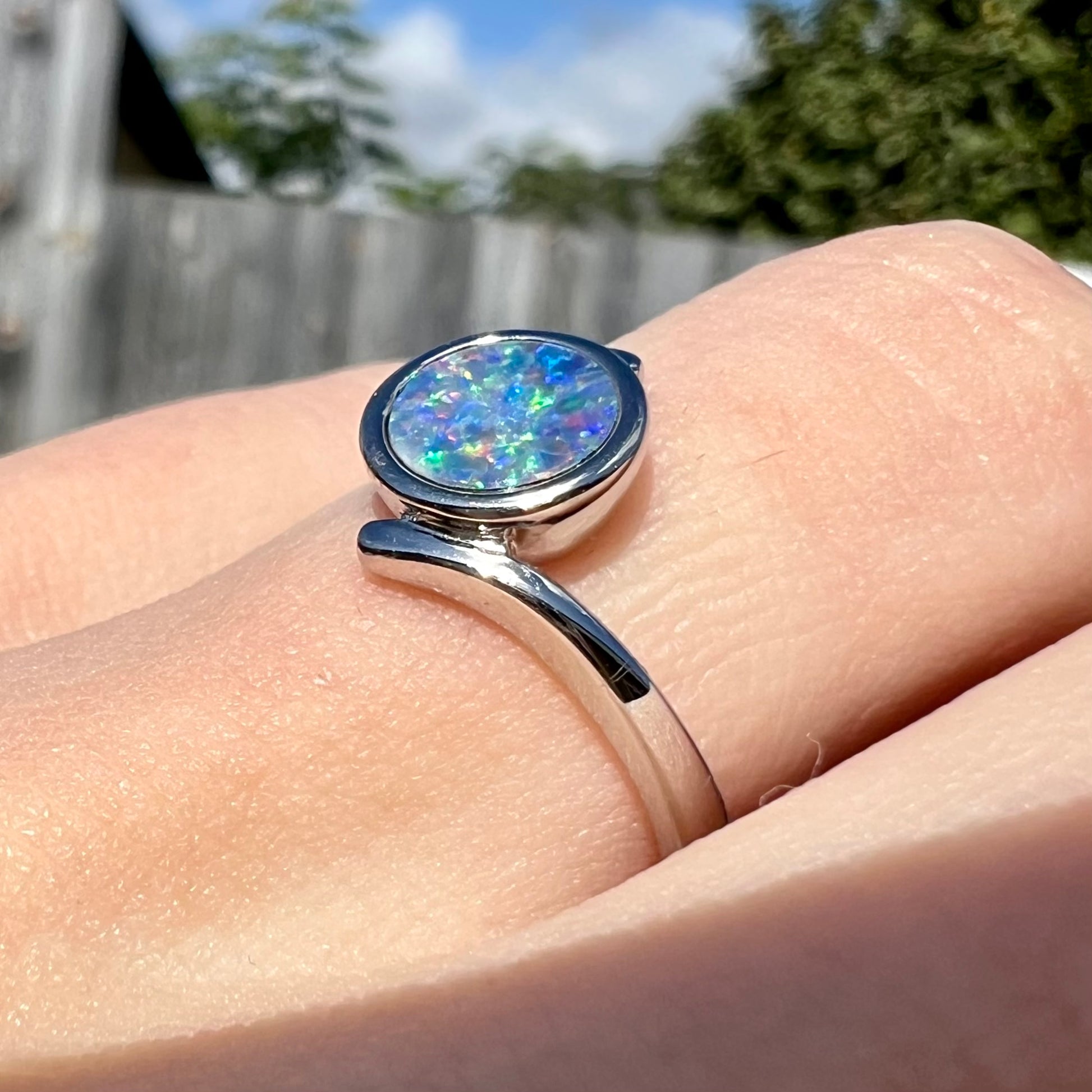 A sterling silver bypass ring bezel-set with a round cut black opal doublet.