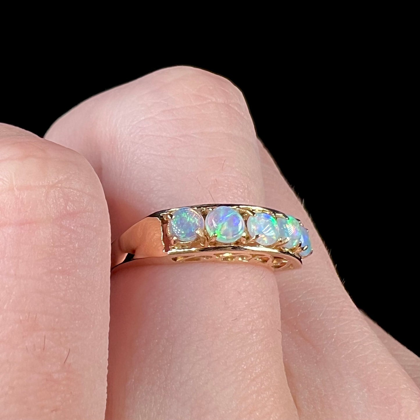 An 18 karat yellow gold line-style filigree ring mounted with five round, cabochon cut Australian crystal opals.