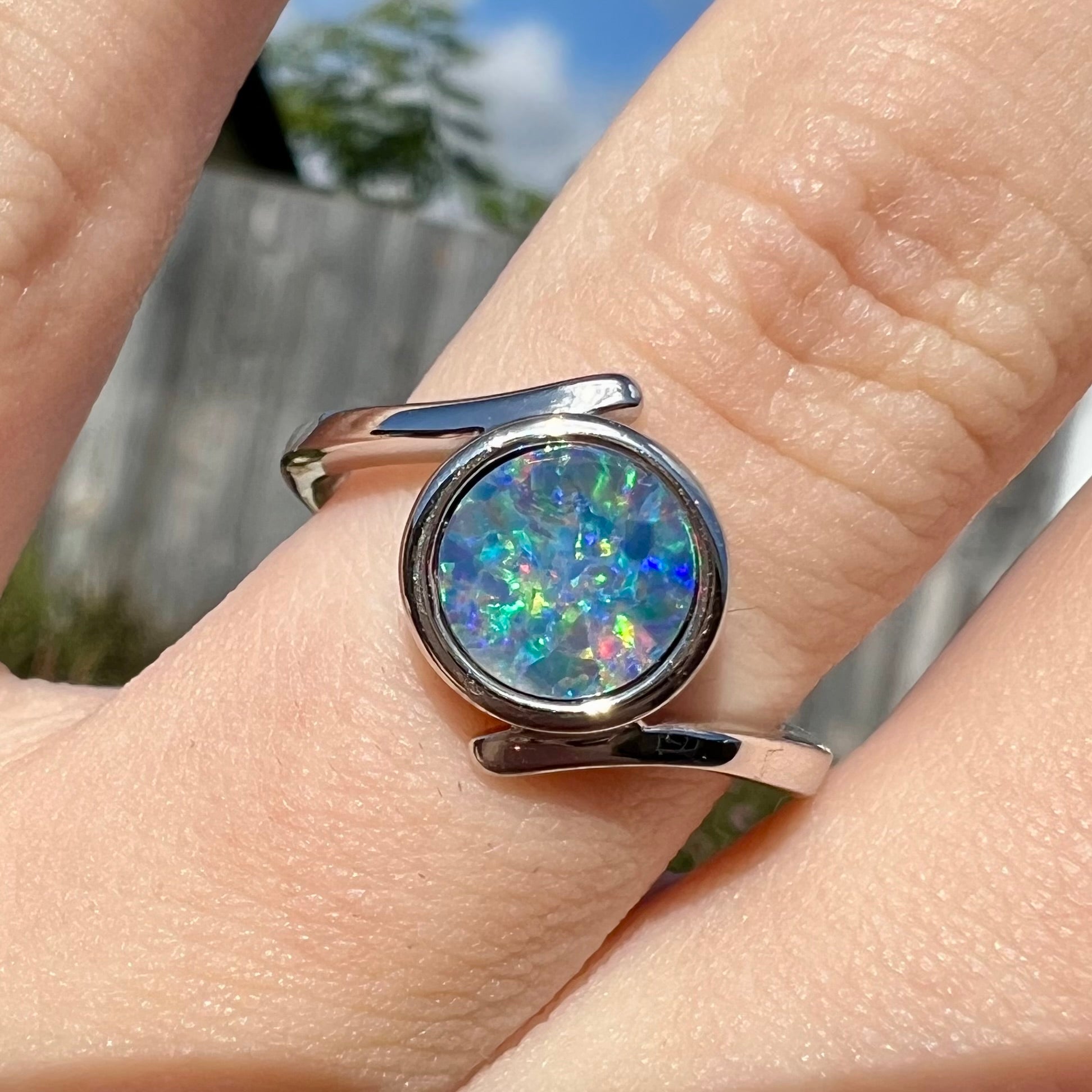 A sterling silver bypass ring bezel-set with a round cut black opal doublet.