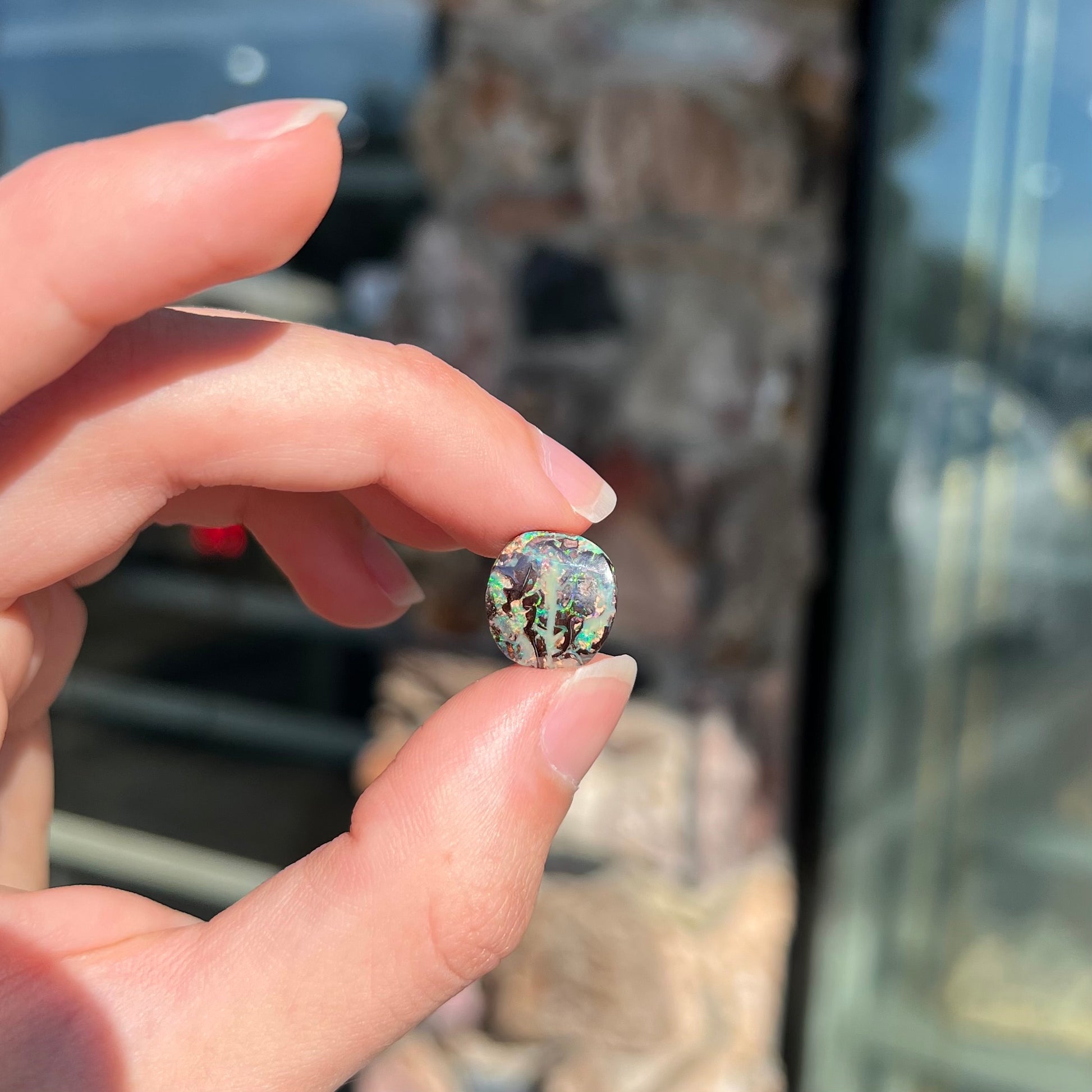 An off-round cabochon cut boulder opal stone from Koroit, Australia.  The opal has green, blue, and red colors.