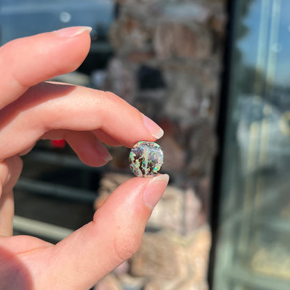 An off-round cabochon cut boulder opal stone from Koroit, Australia.  The opal has green, blue, and red colors.