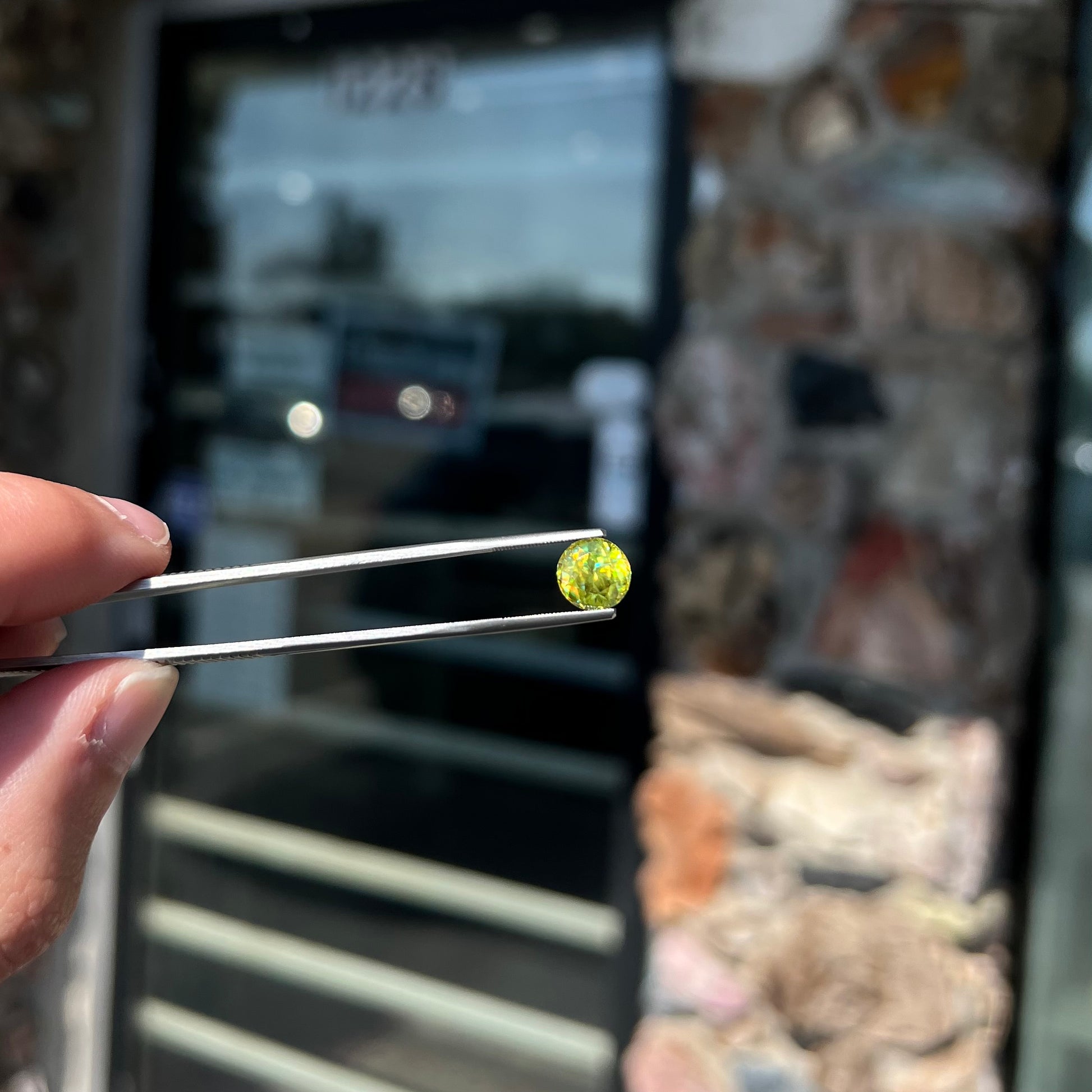 A loose, round brilliant cut sphene gemstone.  The stone is green with orange, green, blue, and yellow flashes.