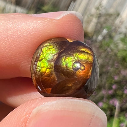 A loose, round Mexican fire agate stone.  The stone shines colors of green, yellow, and orange.