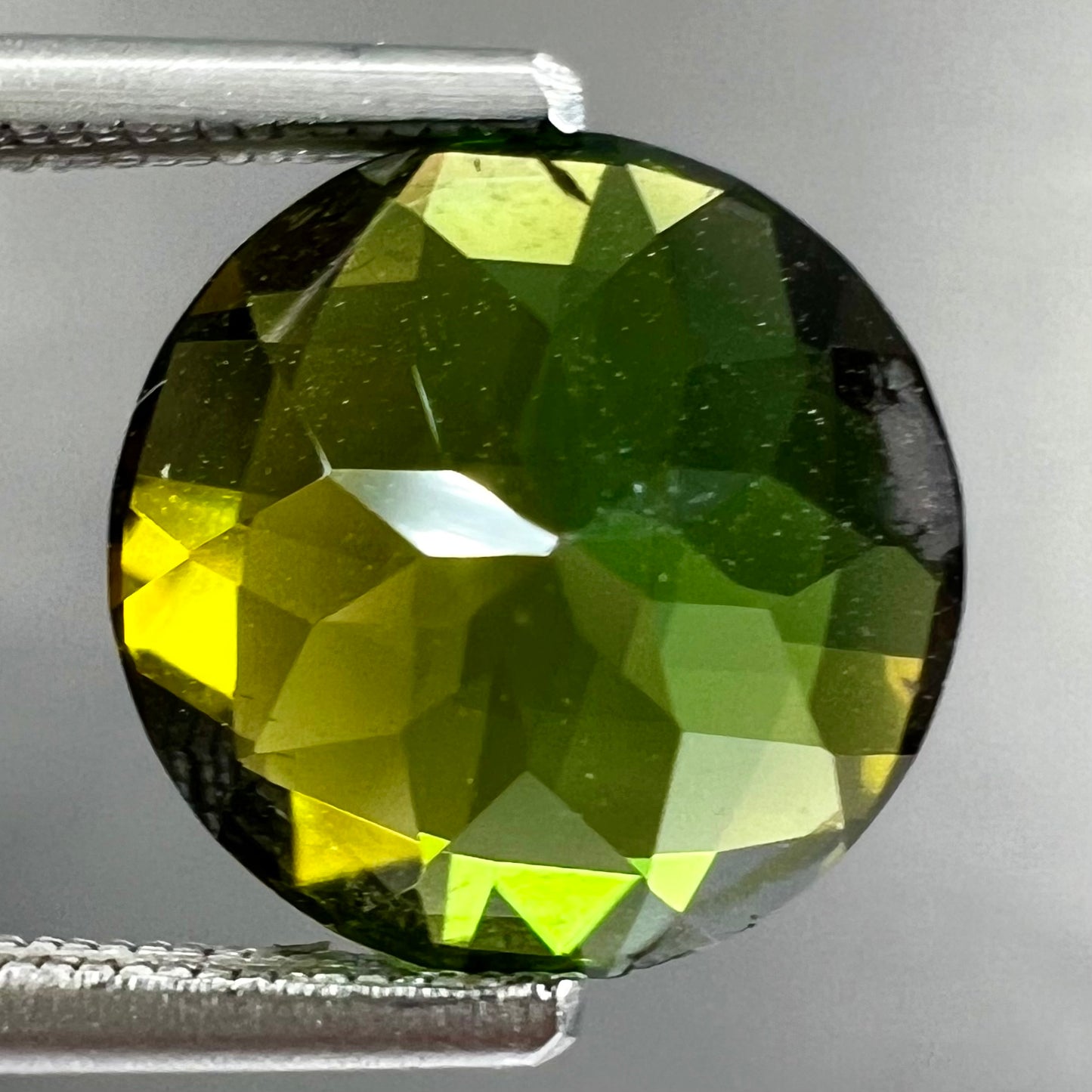 A loose, round checkerboard cut green tourmaline stone with flashes of yellow.