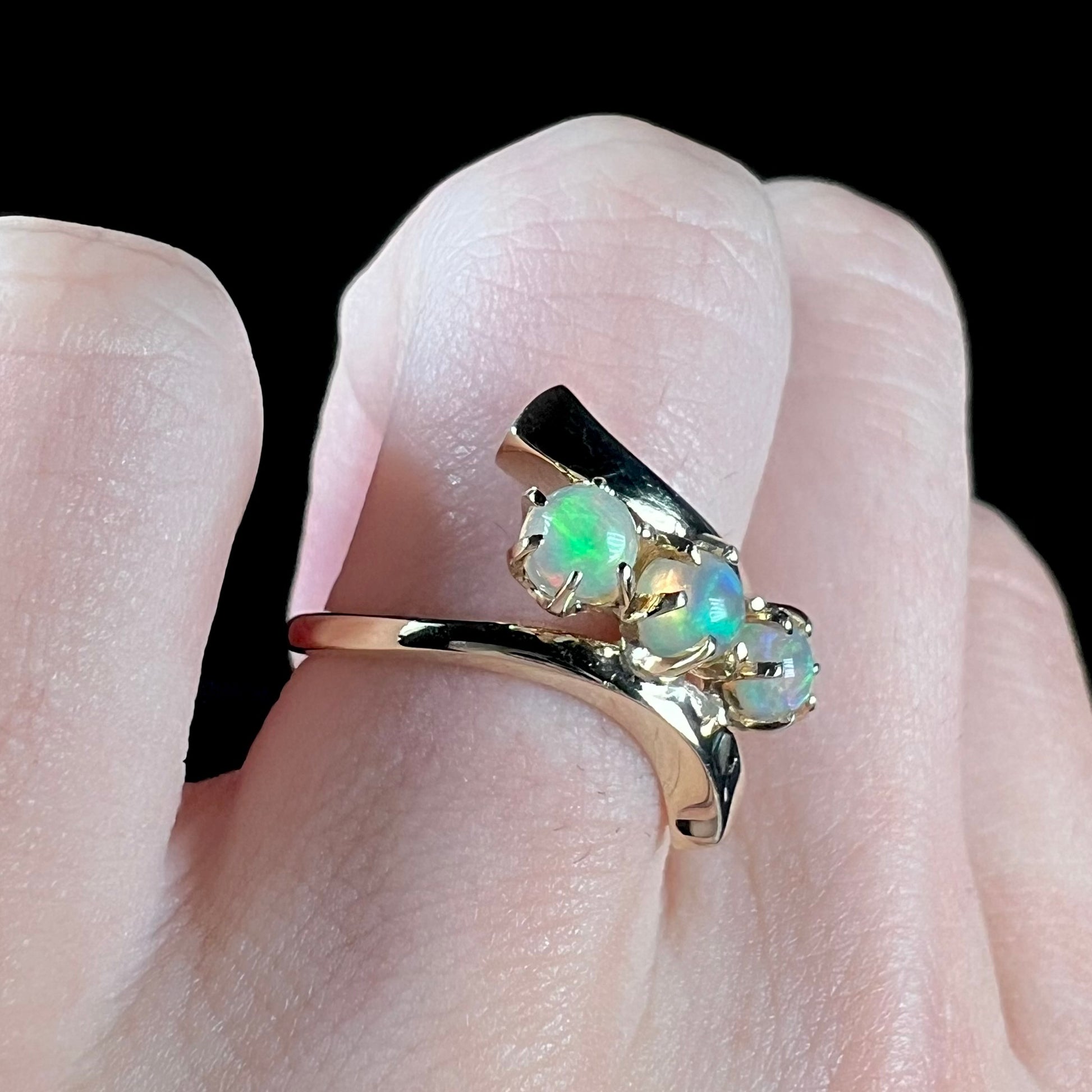 A yellow gold bypass shank ring mounted with three round cabochon cut Ethiopian fire opals.