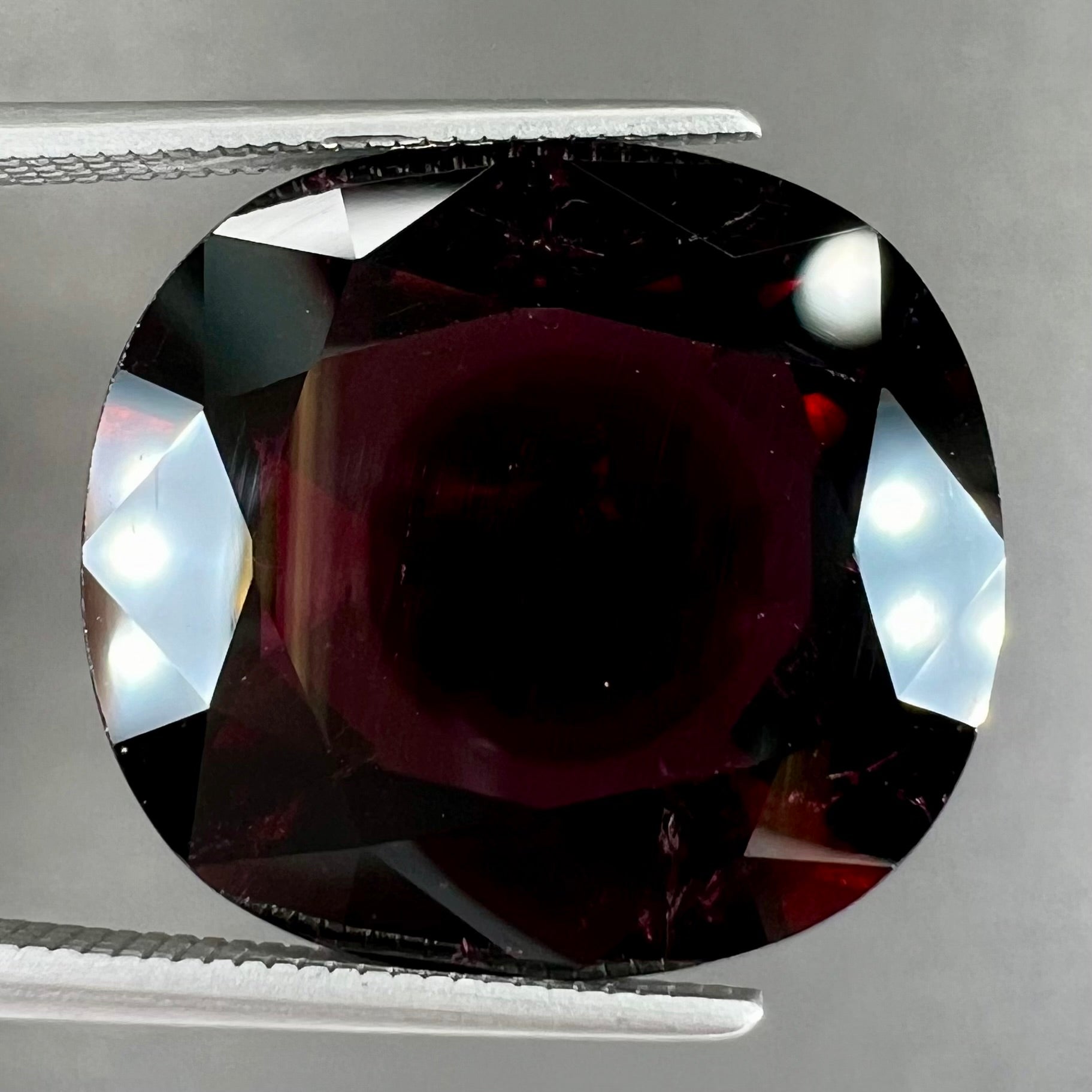 A loose, faceted oval cut rubellite tourmaline gemstone.  The stone is a dark purple red color.