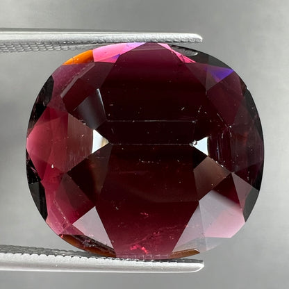 A loose, faceted oval cut rubellite tourmaline gemstone.  The stone is a dark purple red color.