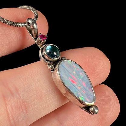 A sterling silver necklace shaped like a child, mounted with an opal doublet, a ruby, and a blue piece of glass.