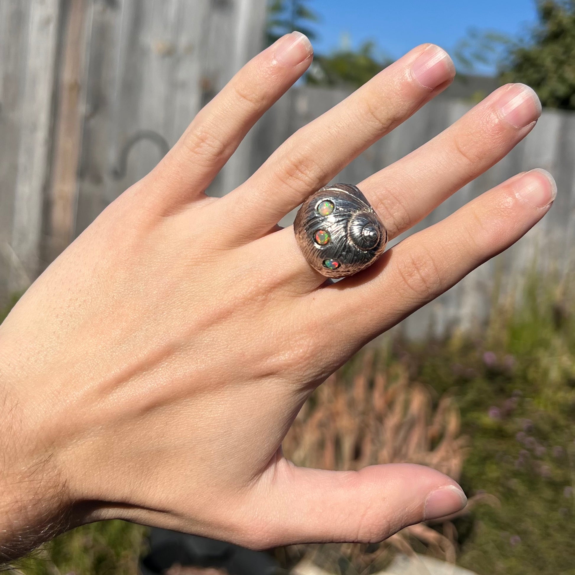 A large, three dimensional sterling silver snail seashell ring set with three round Ethiopian fire opal stones.