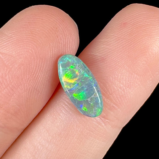 A loose, oval cabochon cut semi-black opal from Lightning Ridge, Australia.  The opal plays green and orange colors.