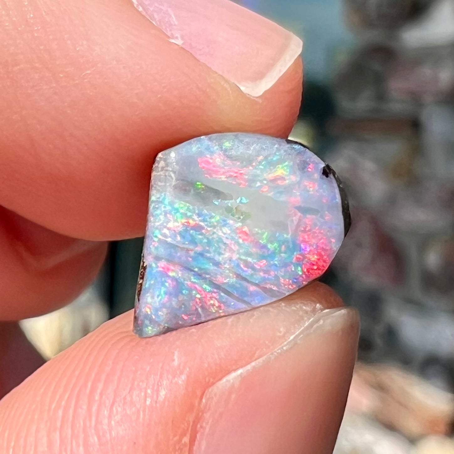 A freeform shaped boulder opal stone with red and blue color play.