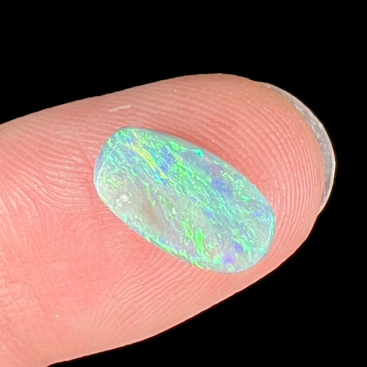 A loose, barrel shaped semi-black opal stone from Lightning Ridge, Australia.  The stone plays green colors.