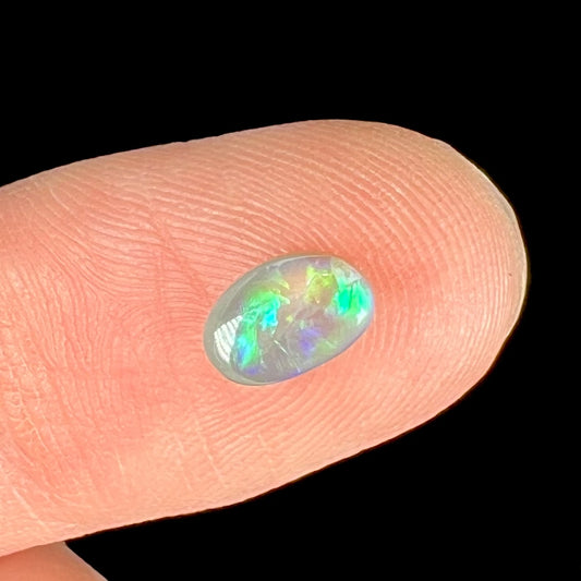 A loose, oval cabochon cut semi-black crystal opal from Lightning Ridge, Australia.