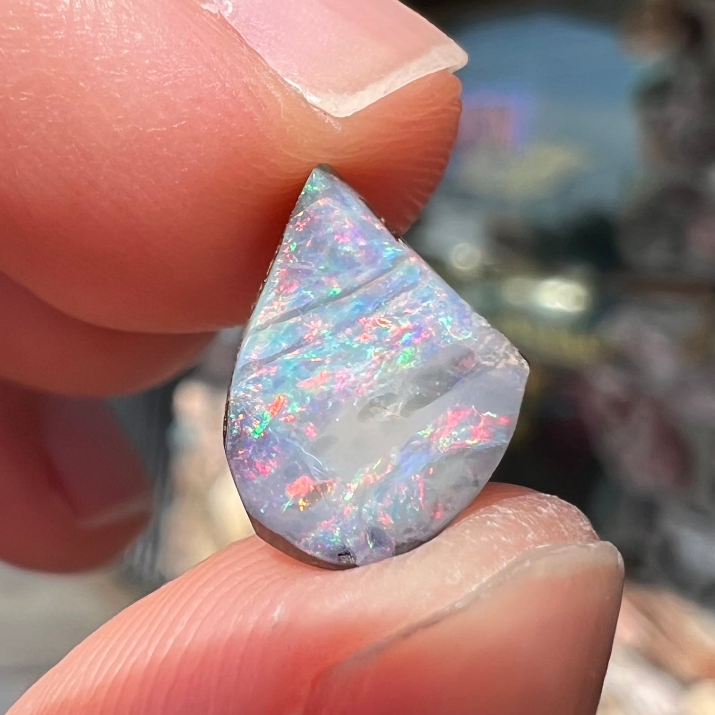 A freeform shaped boulder opal stone with red and blue color play.