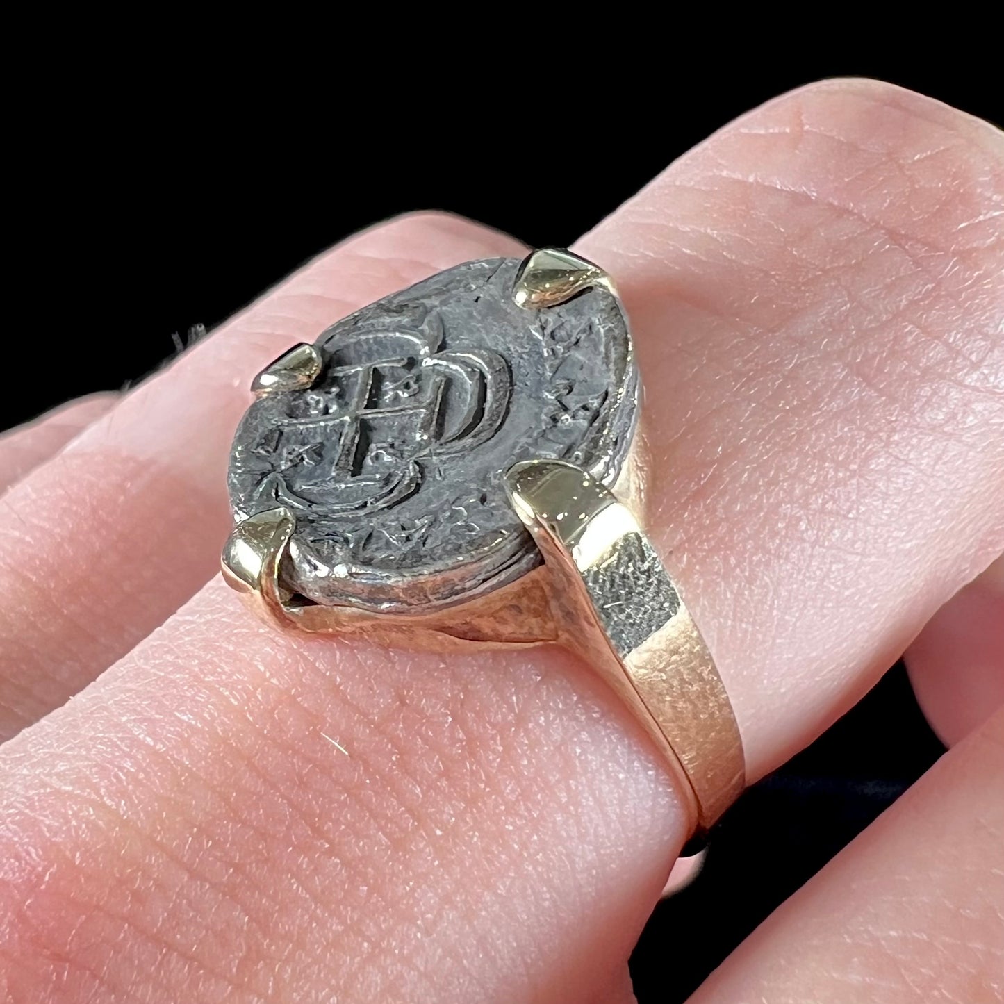 A silver Atocha 1 reale coin replica set in a yellow gold ring.