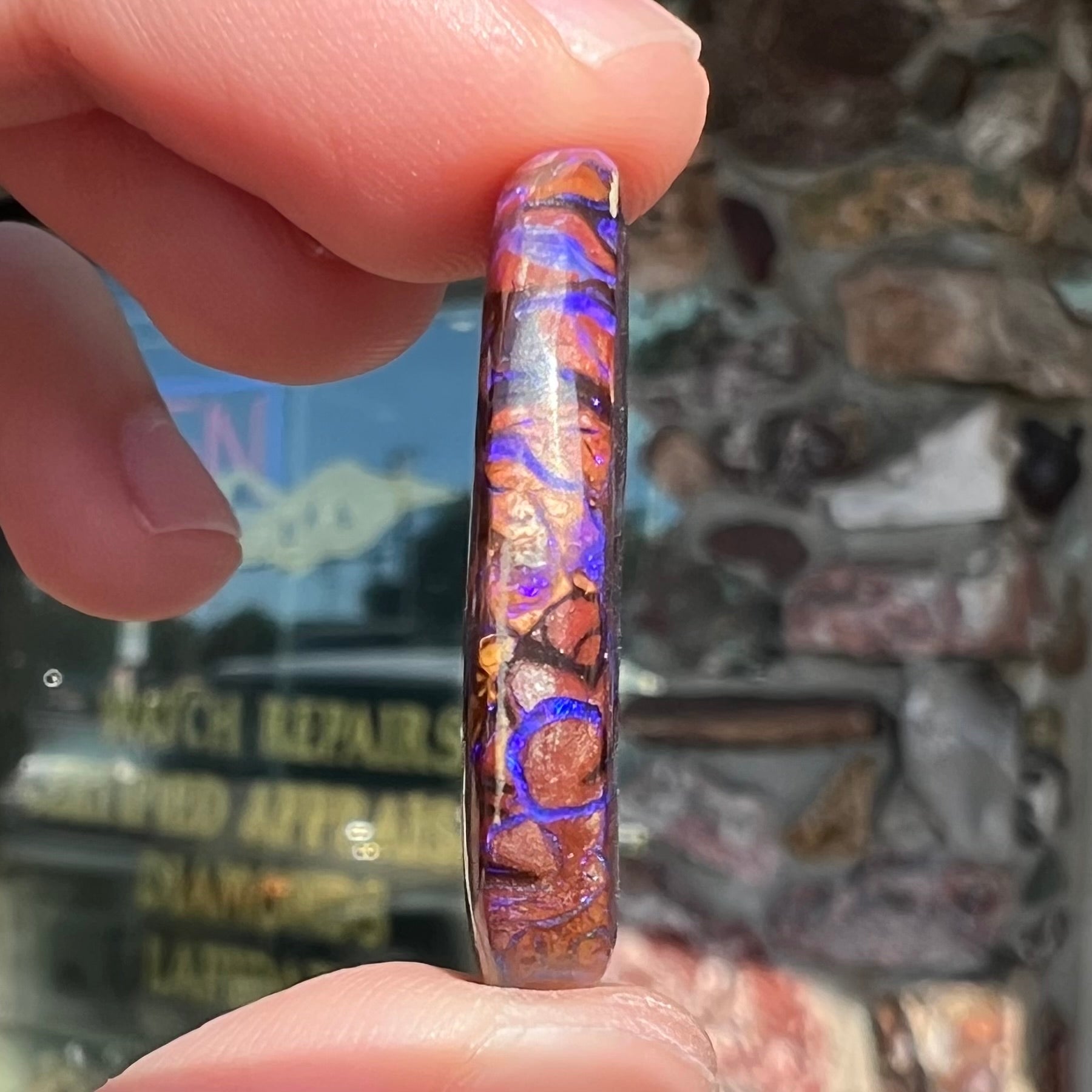 The side of a loose, oval cabochon cut boulder opal from Koroit, Australia.  The opal has violet and purple veins.