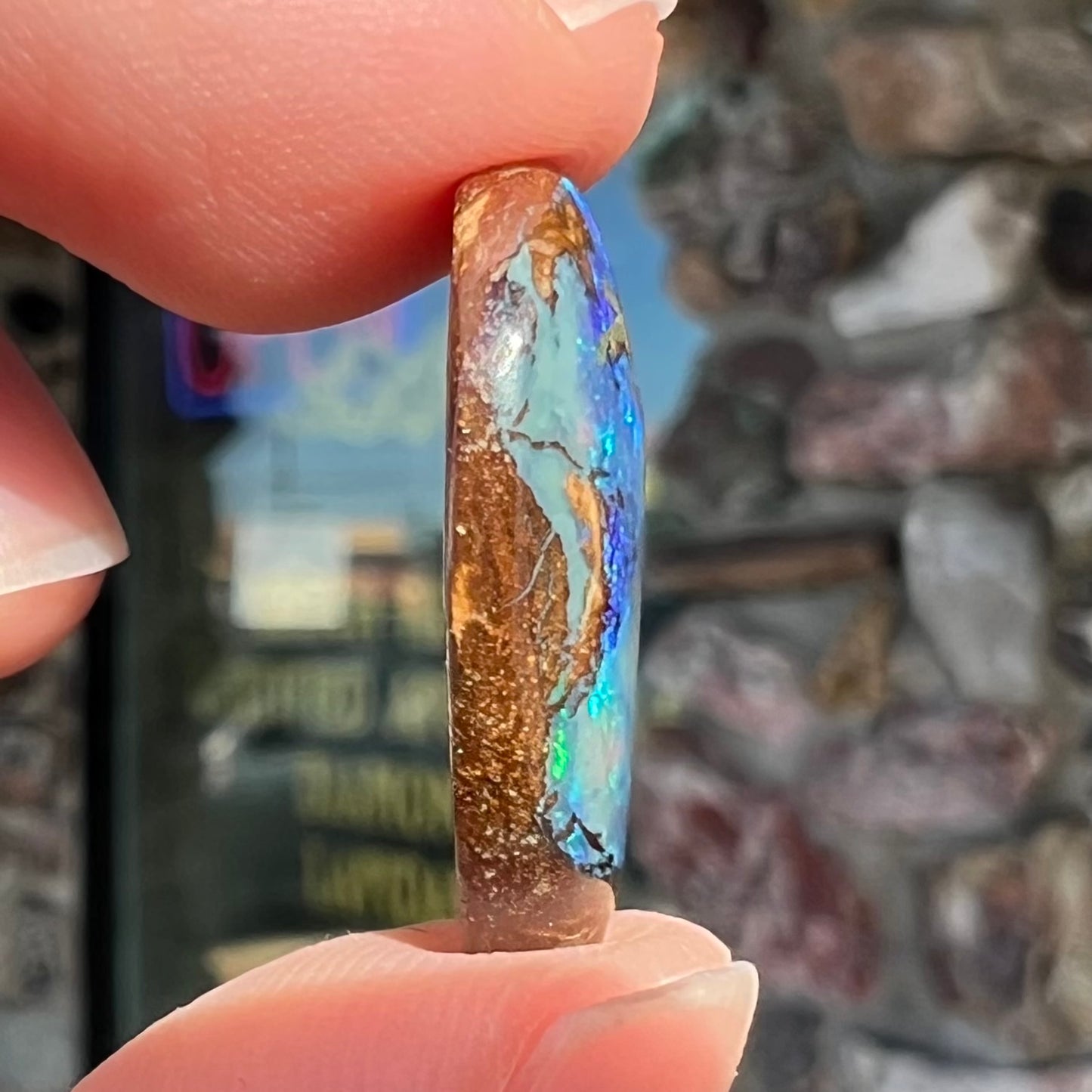 A freeform pear shaped boulder opal stone with blue color.