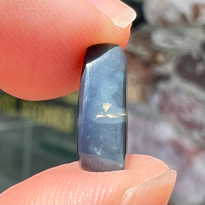 A loose, elongated oval cut black opal that has a green and blue cat's eye.